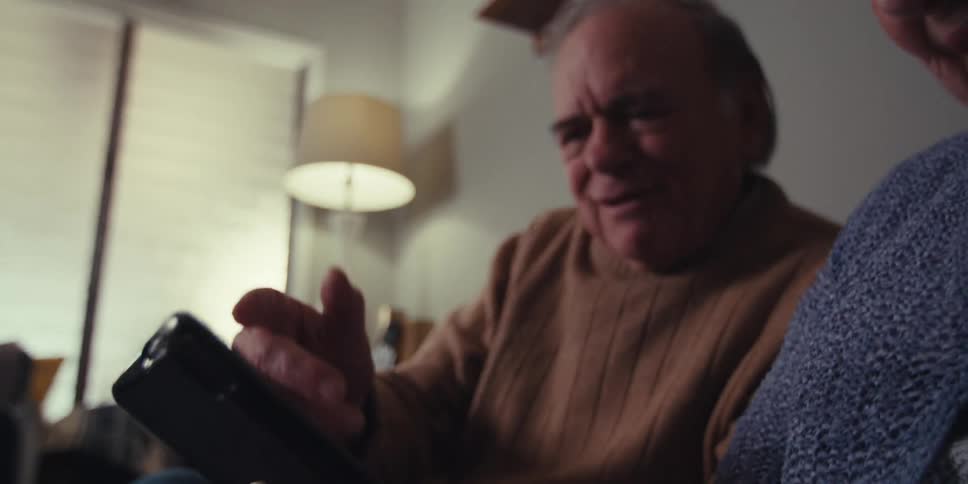 Elderly couple sitting together on a sofa with happy facial expression and interacting with a tablet