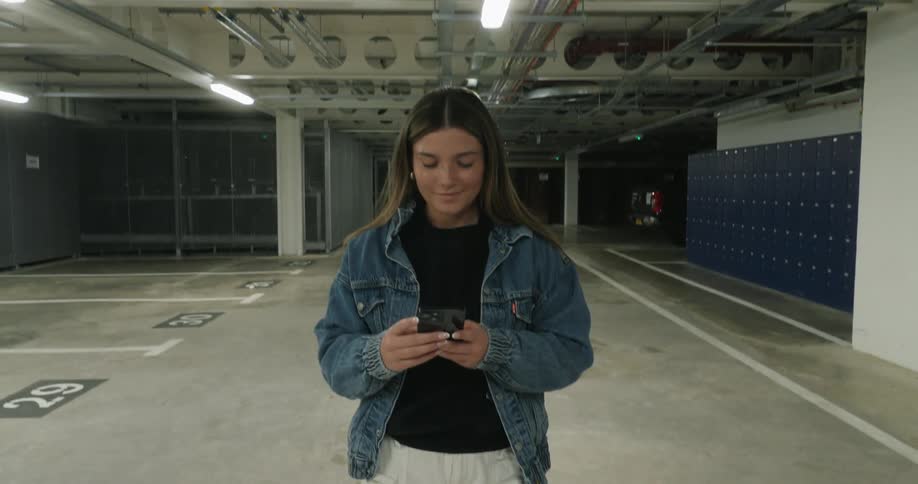 A woman texting on her phone in an underground garage