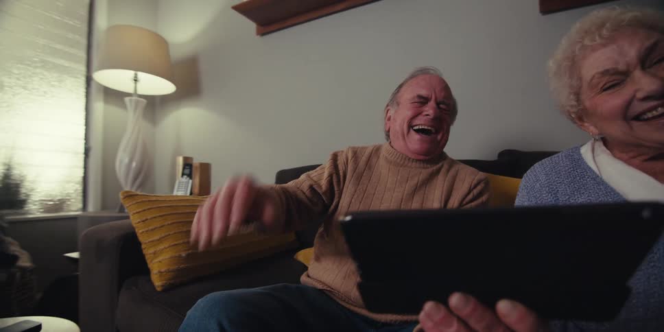 A couple are laughing while they watch the tablet