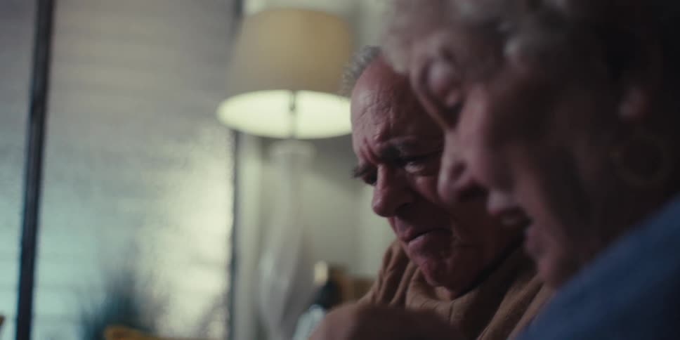 An elderly man and woman sit on a couch using a tablet in the living room