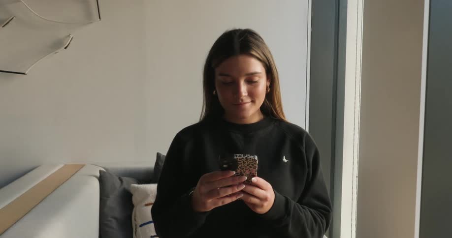 Young woman standing indoors typing on a smartphone