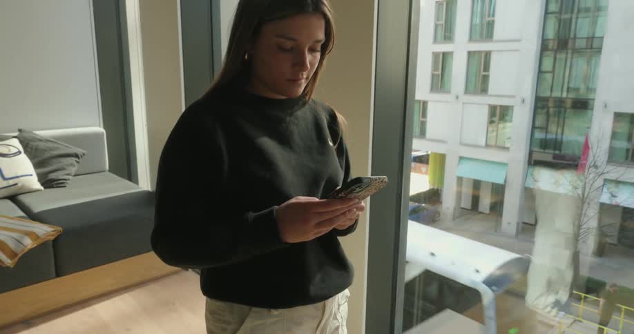A girl is texting near the large window