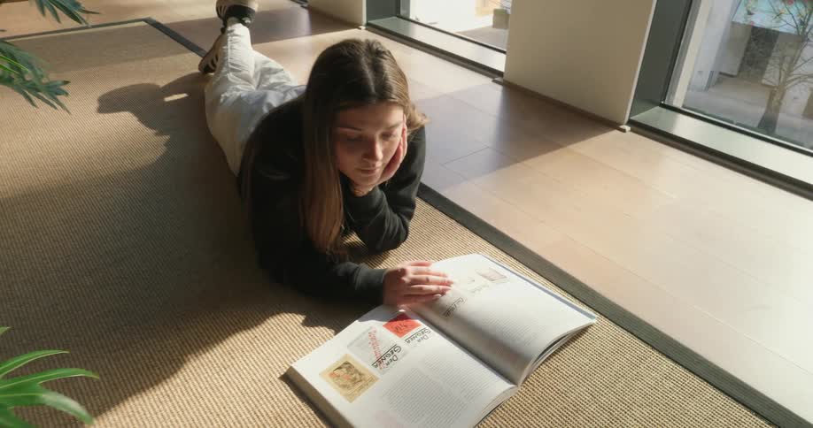 A teenager lays on the carpet reading a book