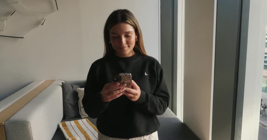 Concentrated young woman standing typing on a smartphone