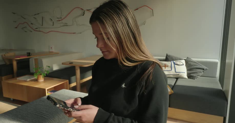 A young woman texting on her smartphone near a glass window