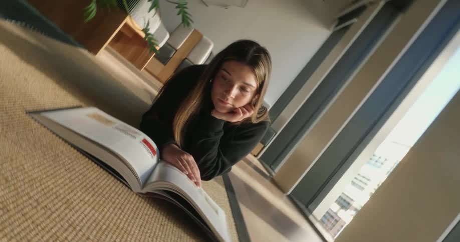 The face of a young girl who is lying on the floor of a living room and reading a book