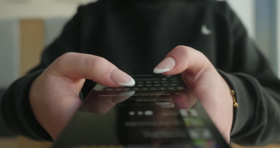 A closeup captures a persons hands holding a smartphone with their thumbs actively typing
