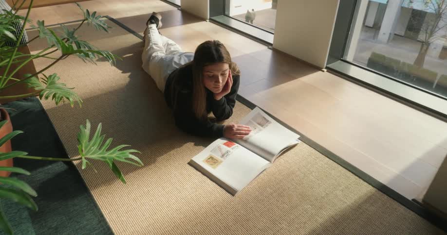 The face of a young woman lying on the floor reading a book