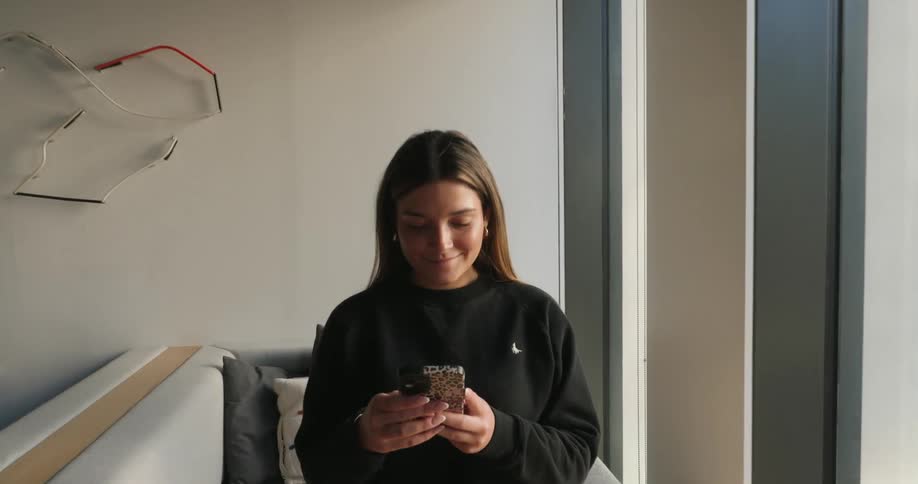 Woman in an indoor space with happy facial expression and interacting with a smartphone