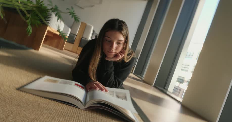 Young woman lying on the carpet of a living room jumping on a book