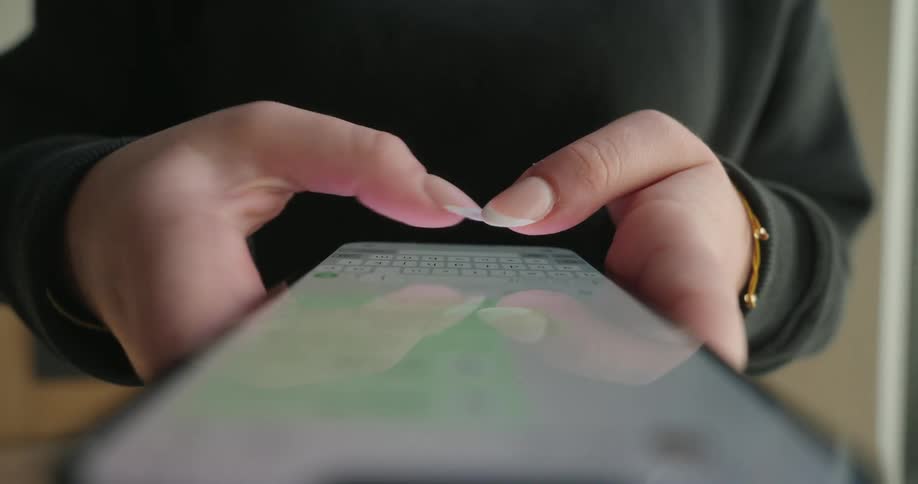 A womans hands typing on a smartphone screen with the focus on the fingers and the screen