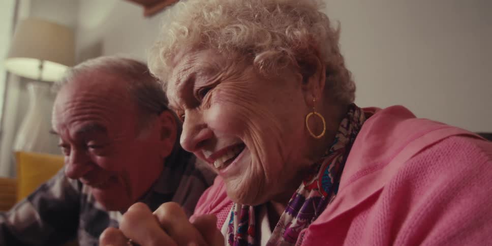 An elderly man and an elderly woman are sitting and looking forward and are very happy paying attention to something in front of them