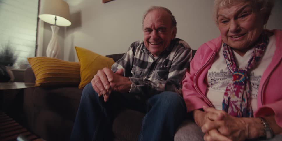 Two elderly people are waving and chatting on a tablet with their relatives