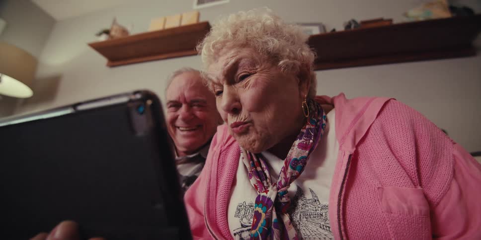 Grandparents sitting on the couch while talking and waving to their relatives on a tablet