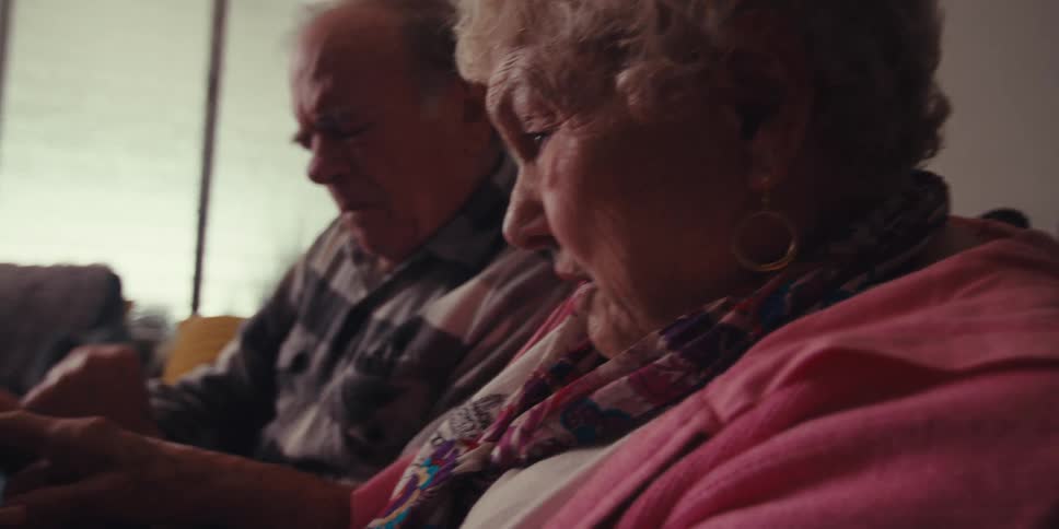 An elderly couple sits together intently examining something on a tablet while lost in thought
