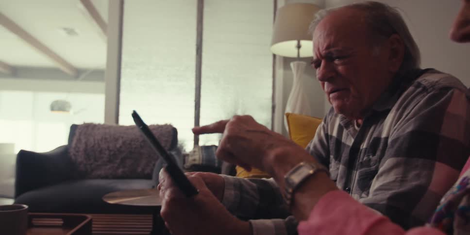 An elderly man and woman use a tablet in the living room at home