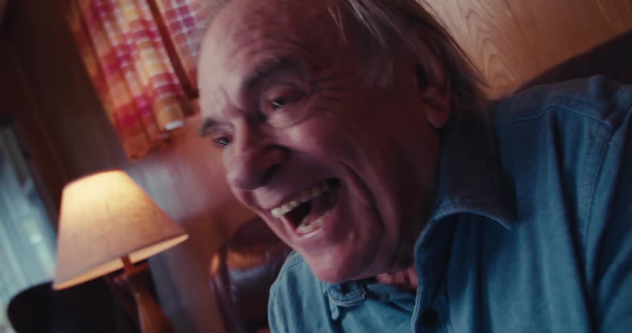 An elderly man is laughing while watching tv in his living room