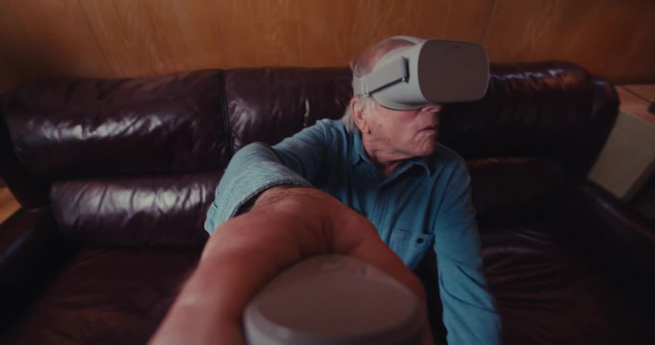 An elderly man relaxes on a leather couch engrossed in a virtual reality experience with a vr headset