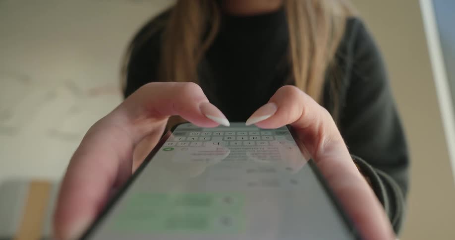 A closeup captures a womans hands holding a smartphone with her thumbs actively typing