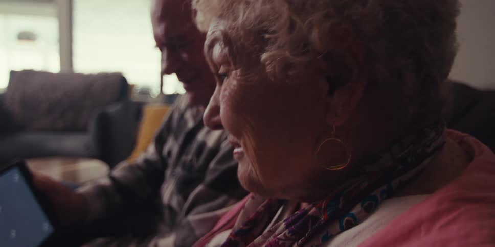 Elderly woman sitting next to a man and laughing as they look at a tablet