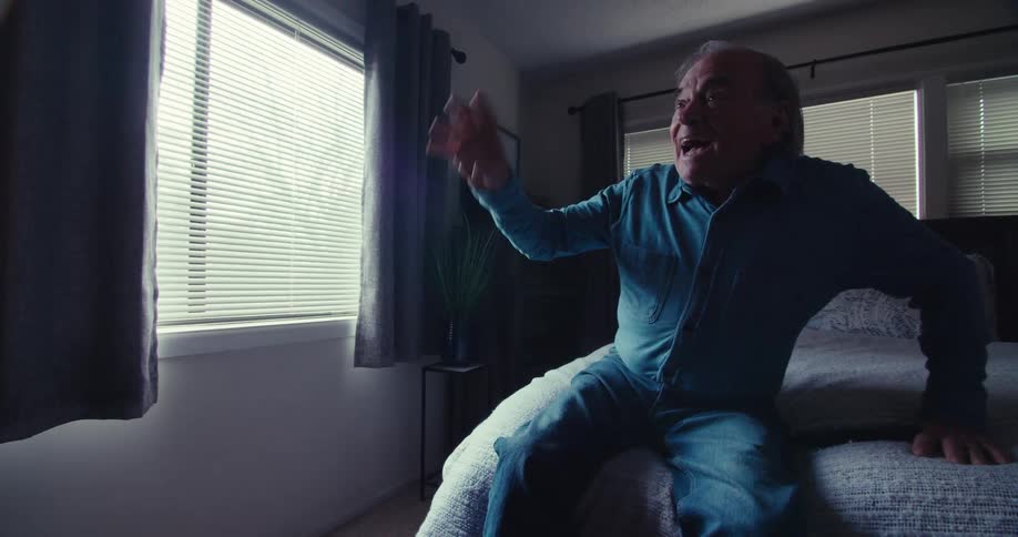 Elderly man sitting on the bed in a bedroom and vibrating happily