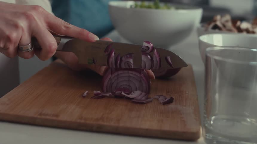 A woman is cutting onions on a chopping board in the kitchen