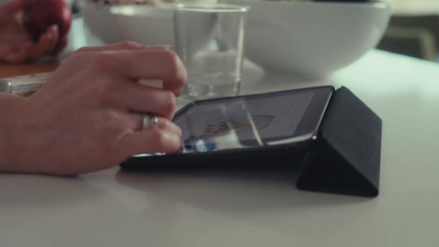 A persons hand using their fingers to move the screen of a tablet on a white table