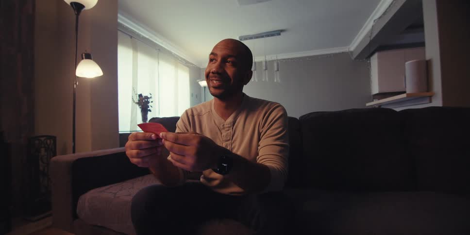 Man holding a red piece of paper and smiling while sitting on a sofa in a living room