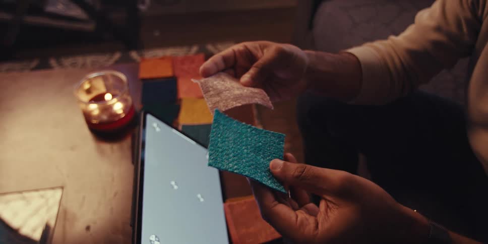 A mans hands are shown holding fabric swatches in front of a tablet