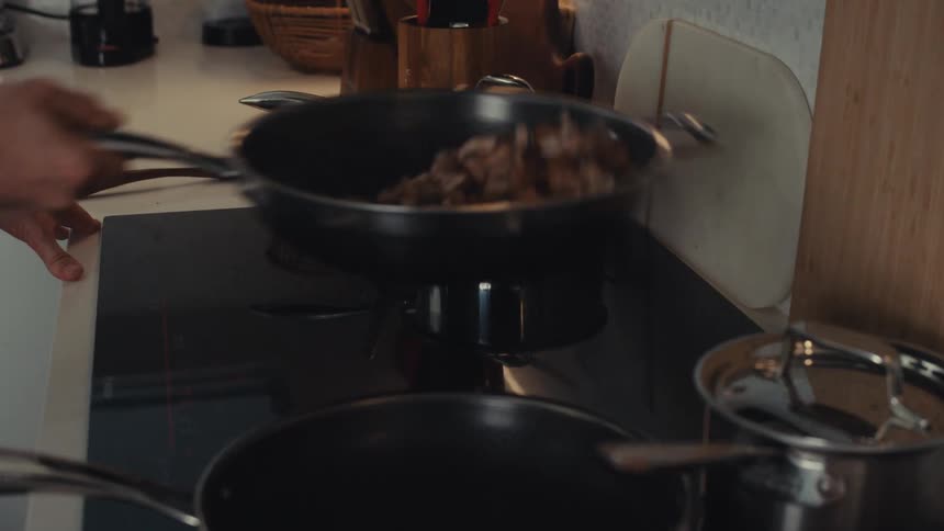 Sauteing mushrooms in a saute pan over a black electric cooktop