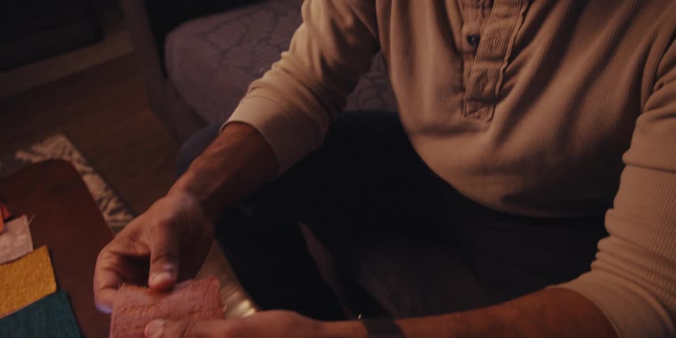 A bald man with a light colored sweatshirt comparing fabric swatches of various colors and textures on a wooden table near a tablet