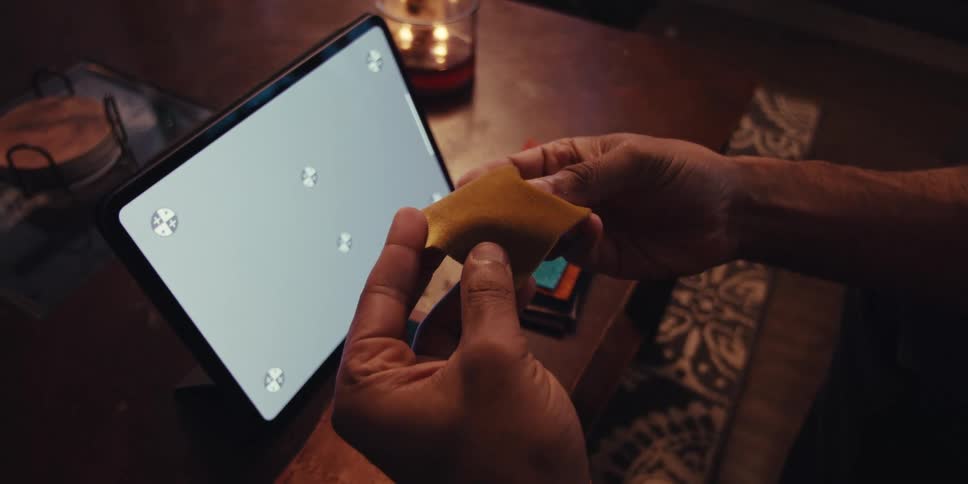 A close up of a man holding rectangular fabric samples in front of a tablet in a dimly lit room