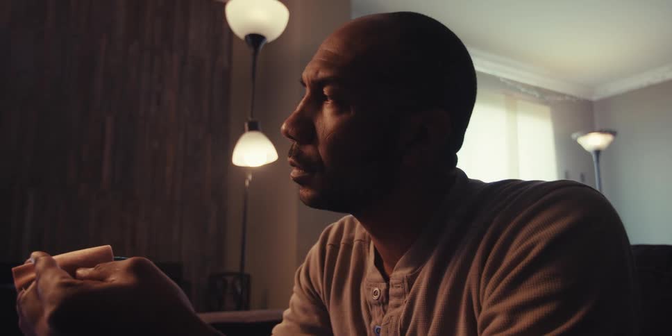 Man sitting in a living room looking thoughtful while holding an object