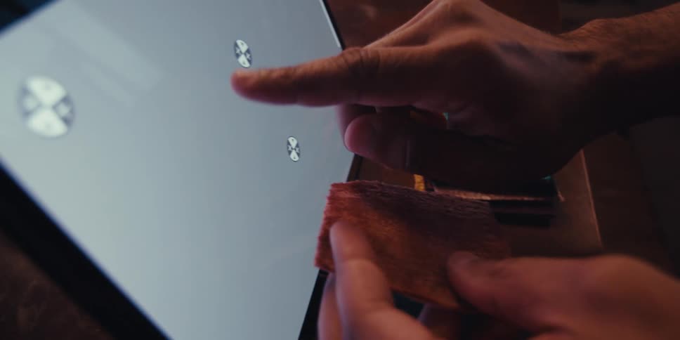 A close up of a hand gesturing toward a tablet with a replaceable screen while holding fabric samples in the other hand