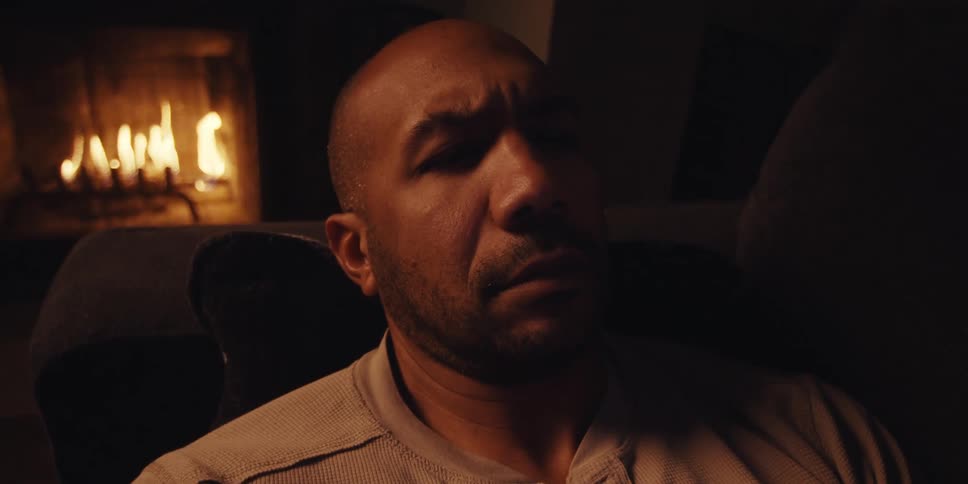 A middle aged mans face illuminated by the warm glow of a fireplace in the background as he looks at his smartphone