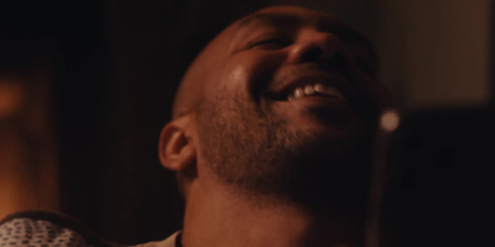 The face of a man who is laughing while looking at his cell phone and behind him there is a fireplace