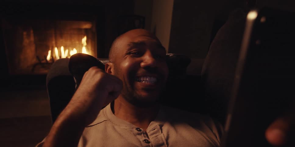 Man relaxing near fireplace enthusiastically cheering watching his team win on cell phone