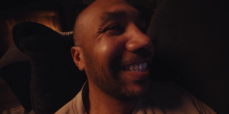 A man rests on a couch smiling excitedly as he looks at his smartphone with a fireplace nearby