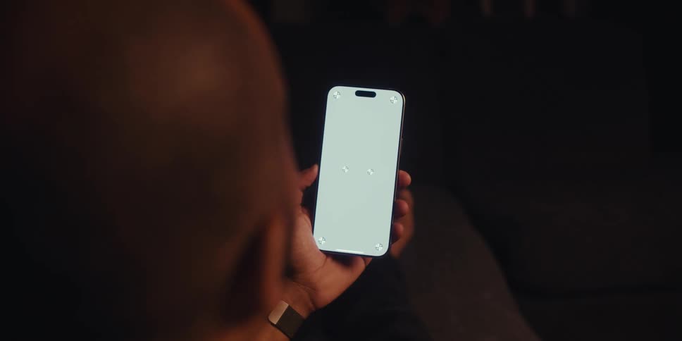 Man sitting in a dark room facing timing on a cell phone