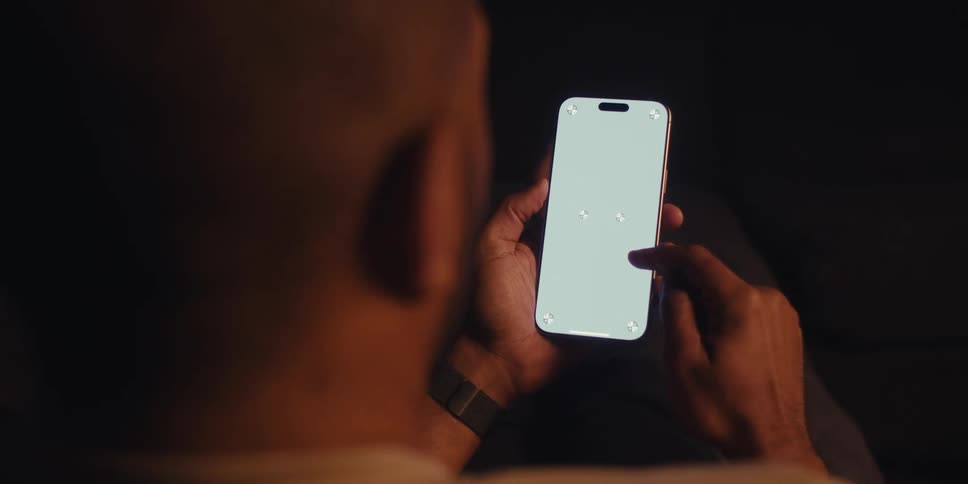 Man sitting in a dark room scrolling on cell phone