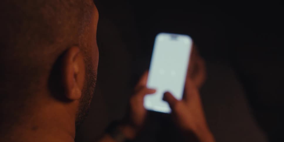 Man sitting in dark room texting on cell phone