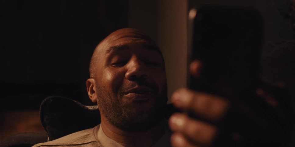 A man sits in a comfortable chair near a fireplace engaged in a video call on his smartphone