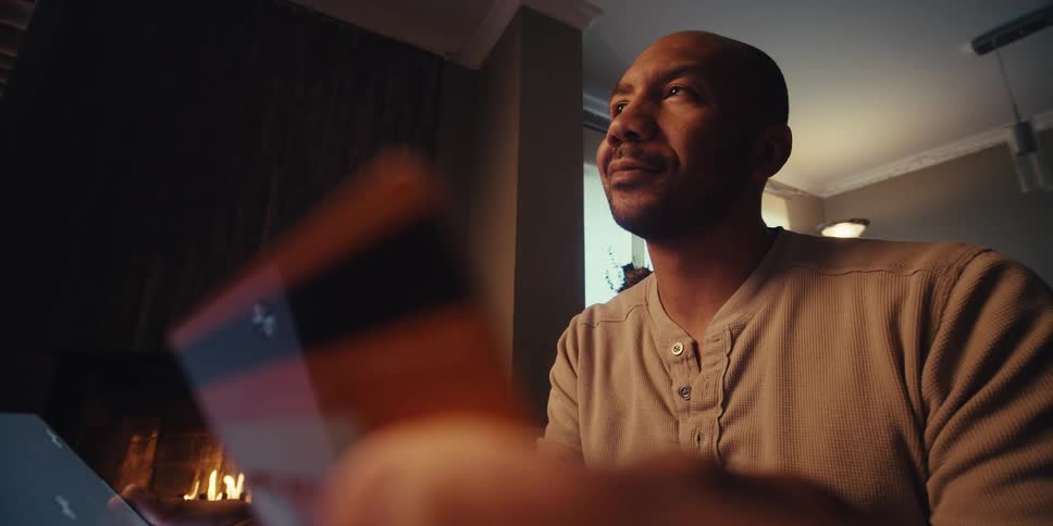 Man looks up and smiles while holding a credit card that reflects the screen of the device he is holding in the other hand