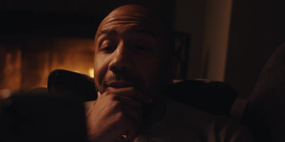 Man lies on the couch in the living room near a lit fireplace and talks during a video call on his smartphone