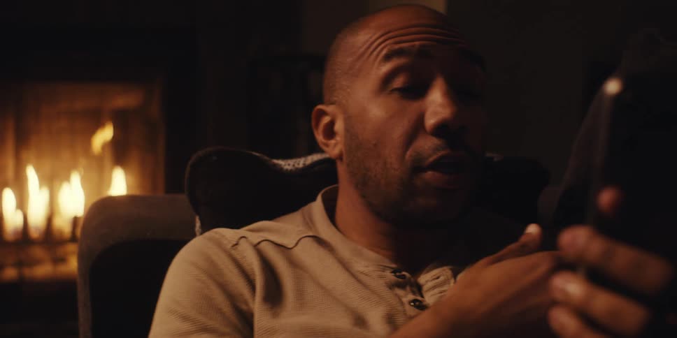 The face of a man who is looking at a cell phone while talking and behind him there is a fireplace