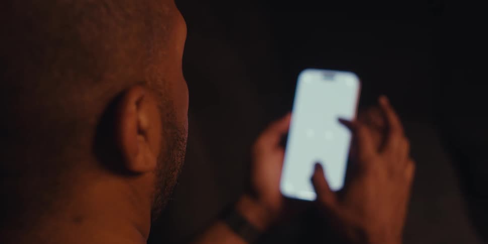 A person is engrossed in their smartphone screen in a dimly lit room
