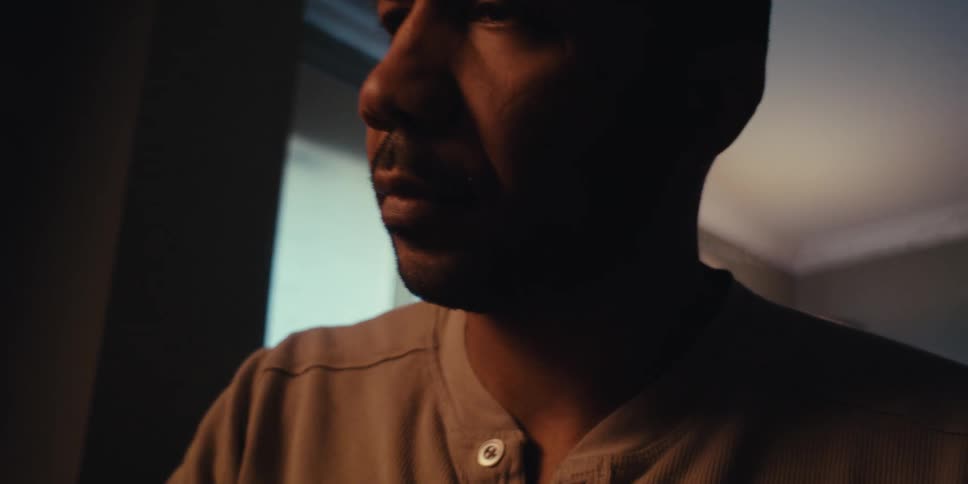 The face of a bald man looking into something in front of him in a partially dark room