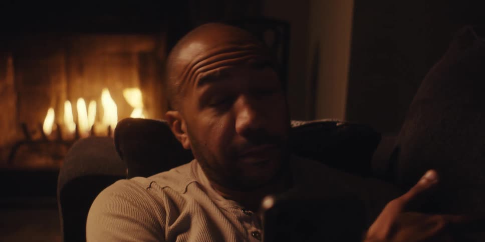 A black man lying on the couch by the fireplace while video calling someone on the smart phone
