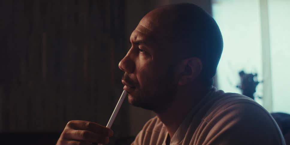 A man sits in a house with a pen in his hand thinking in depth about something