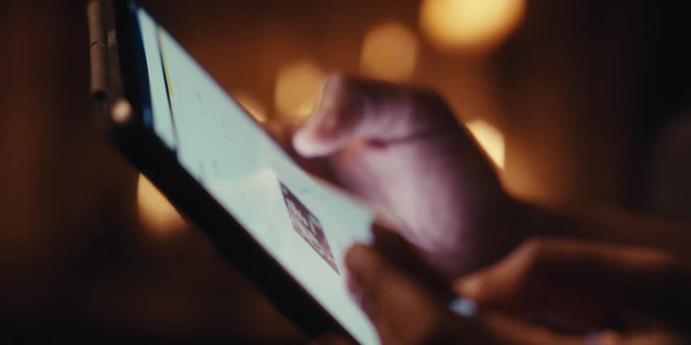 A close up shows a hand holding a credit card while browsing shopping on a tablet near a fireplace in a dimly lit room